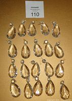 Overview of 20 clear faceted teardrop chandelier crystals with brass pins arranged in rows.