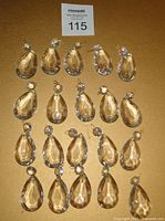 Arrangement of twenty teardrop-shaped clear crystal chandelier drops with brass pins, displayed flat on a surface.