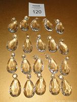 Top-down photo showing all twenty clear faceted teardrop chandelier crystals arranged in rows on a flat surface with lot number.