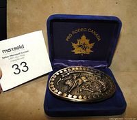 Front view of the official PRO RODEO CANADA solid brass belt buckle resting in its original blue velvet-lined presentation case showing detailed rodeo rider artwork.