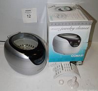 CONAIR ultrasonic jewelry cleaner with clear lid and digital display, original box, and included accessories (jewelry basket, watch stand, CD/DVD holder).