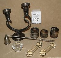 Photo showing silver plated double candle holder, silver plated candle snuffer, three antique silver plated napkin rings, and two clear crystal knife rests on a beige background.