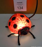 Front view of ladybug lamp lit up showing the stained glass effect and black legs.