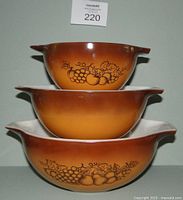 Stacked view of three vintage PYREX Cinderella bowls with Old Orchard fruit pattern in gradient brown-orange color.