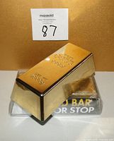Close-up photo of one gold bar shaped novelty door stop showing the gold colored finish and embossing "FINE GOLD 999.9 NET WT 1000G."