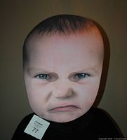 Front view of unusual baby face printed foam mask on black hood showing facial expression and mesh eyeholes.