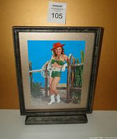 Front view of vintage pinup cowgirl print showing colorful image and Art Deco frame with stand.