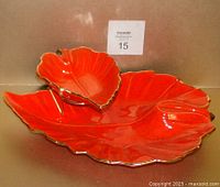 Front side view of the large orange ceramic leaf-shaped serving dish with smaller leaf-shaped dip dish and metal holder on top, showing bright orange glaze and gold edge trim.