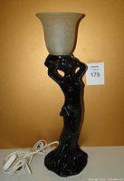 Front view of black ceramic Art Deco goddess lamp with frosted glass shade, showing figure and lamp cord.