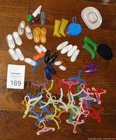 Overview of vintage Barbie and similar doll shoes, boots, hats, a purse, and multiple hangers on a wooden floor surface with a MaxSold card.