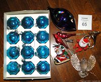 Photo of 12 blue mercury glass ball ornaments boxed, large purple blown glass teardrop ornament, 2 red clip-on bird ornaments, 2 Santa figurines, French horn ornament, and glass dove, arranged on wood floor with lot number.