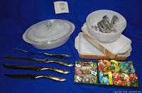 Full view of casseroles, bowl with cookie cutters inside, and carving set laid out on blue background.