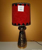 Full view of vintage lamp with red velvet shade and black scalloped trim against ochre background