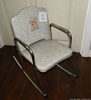 Full view of grey cracked ice vinyl children's rocking chair with chrome frame on wood floor.