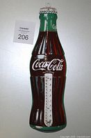 Front view of vintage Coca-Cola bottle-shaped metal thermometer showing colorful logo and thermometer tube.