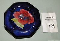 Front view of octagonal ashtray with red hibiscus flower on deep blue background, showing vibrant colors and glaze.