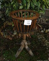 Front-side angle showing the wooden spindle basket and tripod base on a natural ground setting with plants in background.