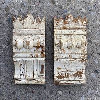 Front view of pair of distressed antique wooden door corner blocks on concrete surface.