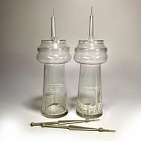Pair of vintage CN Tower cocktail glasses with removable CN Tower shaped lids and two metal Top of Toronto swizzle sticks laid out on surface
