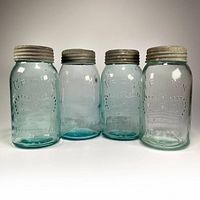 Four antique embossed blue glass Crown Imperial 1 quart sealer jars with metal lids in a row.