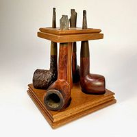 Four vintage tobacco pipes displayed in the wooden pipe rack, showing pipe bowls and missing stems