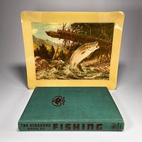 Photo showing the fishing-themed serving tray standing upright behind the hardcover book lying flat, showing both items together.