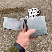 Frontal view of the lighter held in hand showing open lid and perforated chimney.