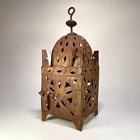 View of the candle holder showing its geometric and floral perforations, domed top with hanging loop, and rustic metal finish.