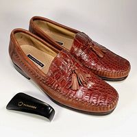 Pair of men's brown Florsheim Imperial slip-on loafers made with genuine cayman alligator leather and leather lining and soles. Includes a black Florsheim-branded shoe horn shown beside the shoes.