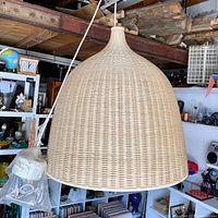Large dome-shaped hanging rattan pendant lamp suspended showing full lamp and some background items.