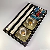 Photo showing full original packaging with two white candles, two brass-colored candle holders, and instruction manual.