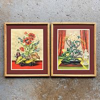 Pair of vintage Asian-themed floral prints in bamboo-style frames on a concrete floor.
