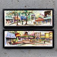 Pair of framed hand-painted porcelain tiles showing Parisian streetscapes, Moulin Rouge and Champs Elysees, in black frames on concrete surface.