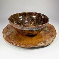 Serving bowl placed on the ceramic serving tray showcasing the textured and iridescent raku-style glaze of both pieces.