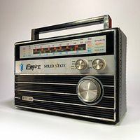 3/4 side view of vintage Empire solid state 4-band portable radio showing tuning dial, volume and band selector knobs, 'Instant Sound' branding, and carrying handle.