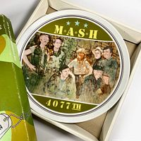 Ceramic round plate with an illustration of M*A*S*H TV series cast, text 'M*A*S*H 4077th', in original box with certificate of authenticity.