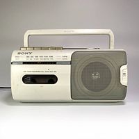 Front view showing radio dial, cassette compartment, speaker grill, control buttons, and handle