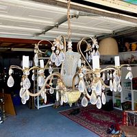 Full view of vintage brass chandelier with 5 arms and many hanging crystal drops, illuminated by natural light in garage setting.