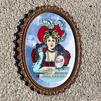 Front view of vintage oval Coca-Cola mirror showing the woman holding a glass of Coke and the 5 cent sign, ornate decorative frame detailed around the edges