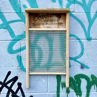 Front view of the vintage washing board showing the wooden frame, glass scrubbing surface, and printed branding partially faded at the top.