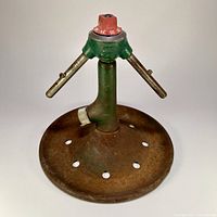 Front view of the entire lawn sprinkler, showing the circular base, green body and metal arms with red dial on top.