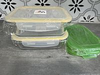 Two clear glass casserole dishes with yellow-sealed locking lids stacked, plus two green replacement lids separately wrapped.