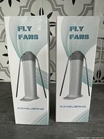Two boxed fly fans shown upright against a patterned background, boxes labeled 'FLY FANS' with brand 'KINGUIBANG'.