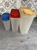 Three Tupperware dry storage containers in varying sizes with lids on a countertop.
