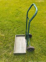 Side angle showing green metal frame cart with wooden base and two black wheels on grass