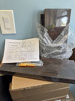 Photo of stacked wooden floating shelves with dark stain finish, one box shelf and two flat plank shelves visible. Assembly instructions and hanging hardware on top.