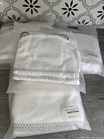 Photo showing folded white hooded towel with gray striped border and small ears on hood, with packaging bags visible underneath