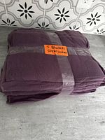 Five purple fleece blankets folded and stacked with an orange label stating 5 blankets 50x60 inches.