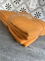 Folded stack of five orange fleece blankets with tape securing the blankets together, shown on a countertop with tile backsplash and outlet.