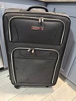 Front view of large black suitcase with two zippered pockets and Air Canada logo badge on front.